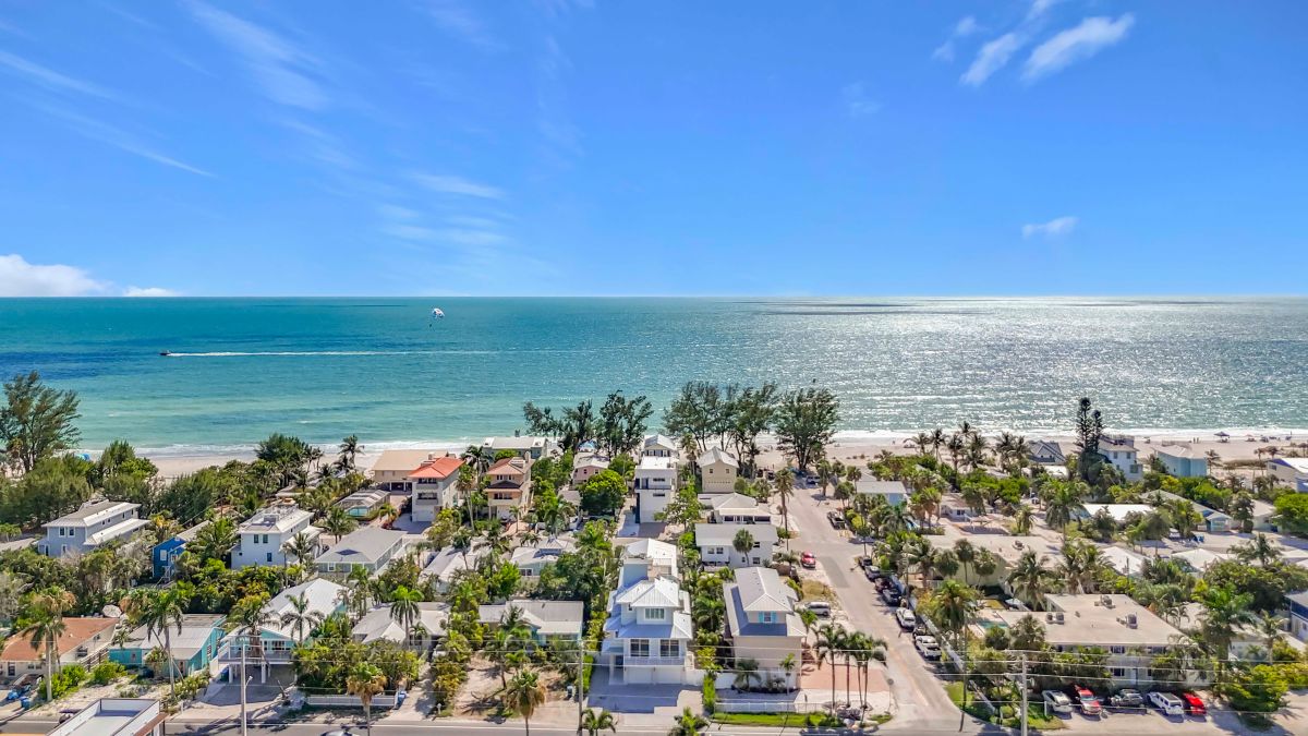 An aerial view showcasing beachfront vacation homes nestled among tropical palms, with the turquoise ocean stretching to the horizon on a sunny day.