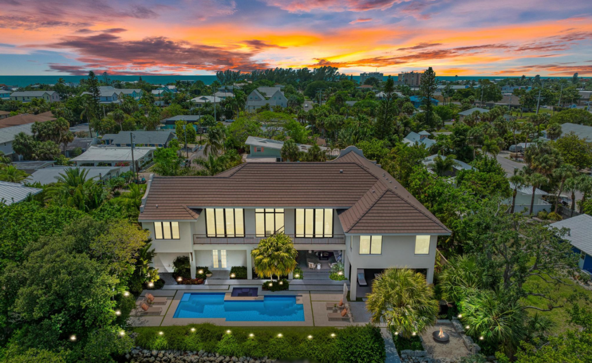 An aerial view of the vacation rental at sunset, showcasing the main building, pool, and surrounding palm-filled neighborhood—a perfect coastal retreat awaits.
