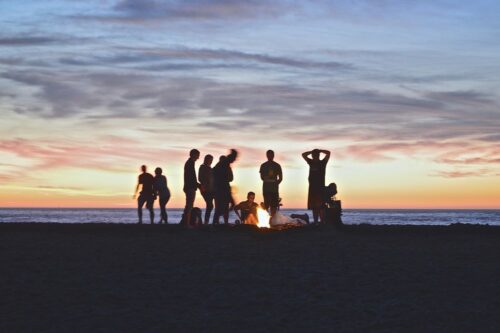 people standing around a campfire on the beach